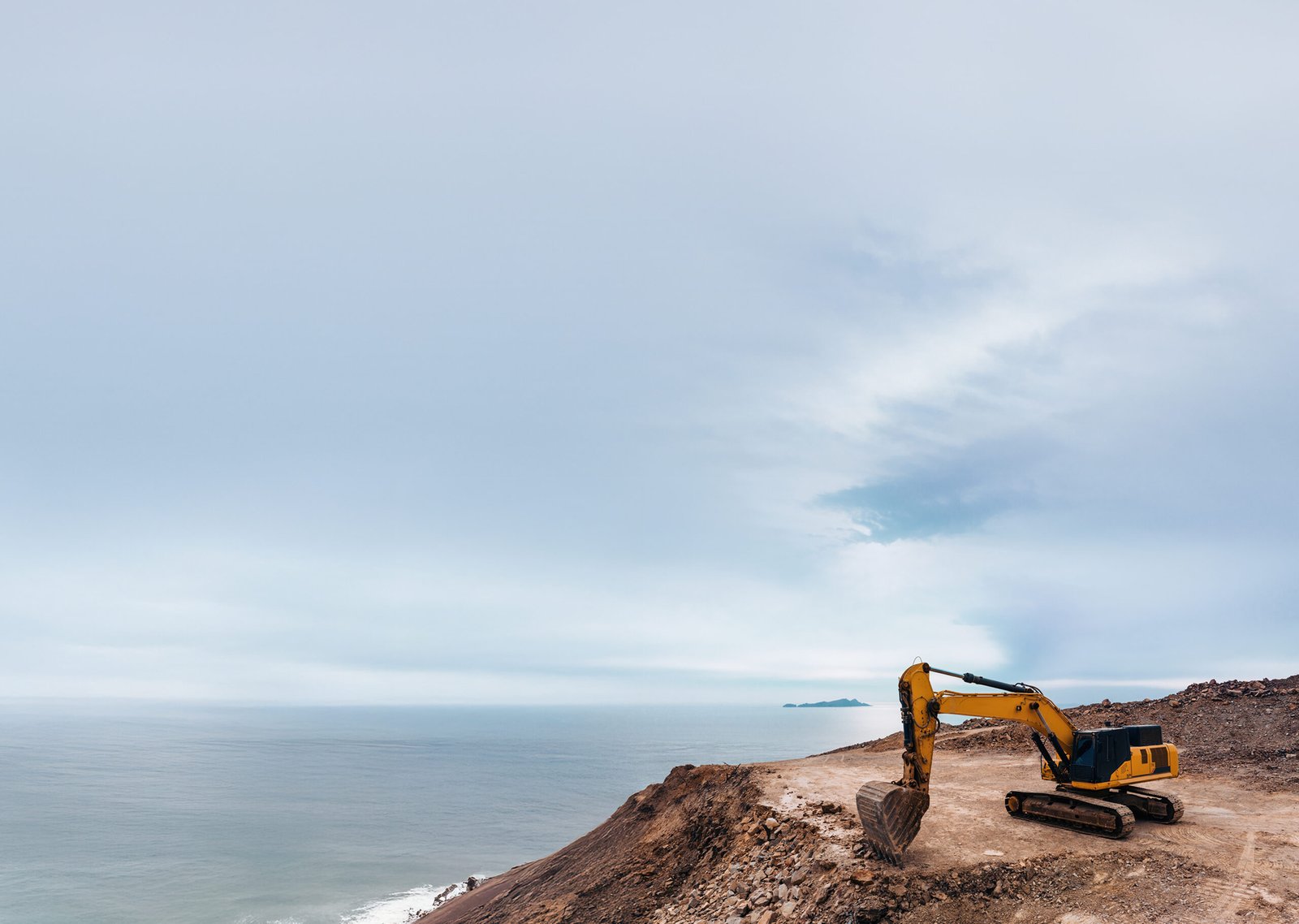 A wide sky shot of an excavator on a cliff edge.