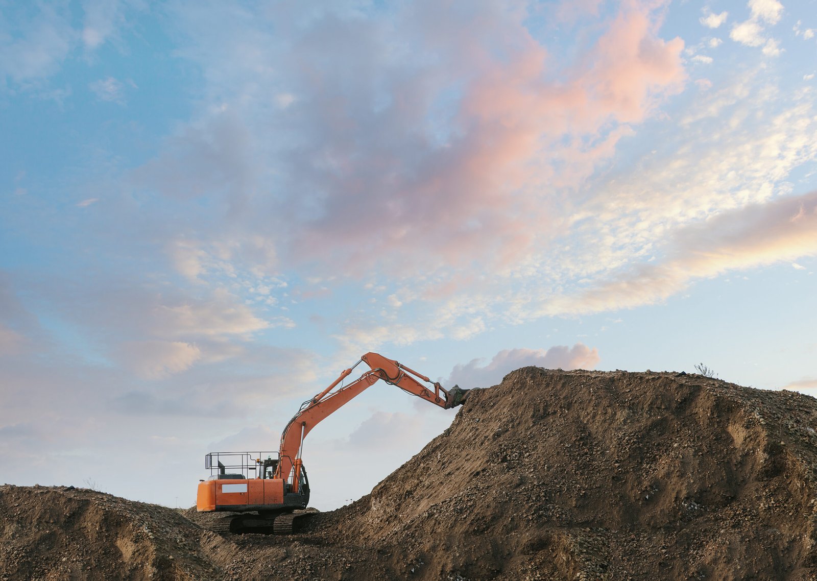 An excavator reaching to the top of a pile of earth.